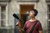 A man wearing headphones holding a condenser microphone inside a building