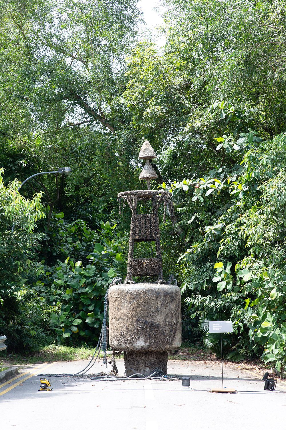 Encrusted navigational buoy on a road surrounded by forest.