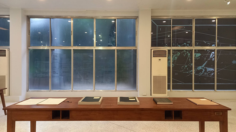 A room with a table of books and windows featuring images and grids.