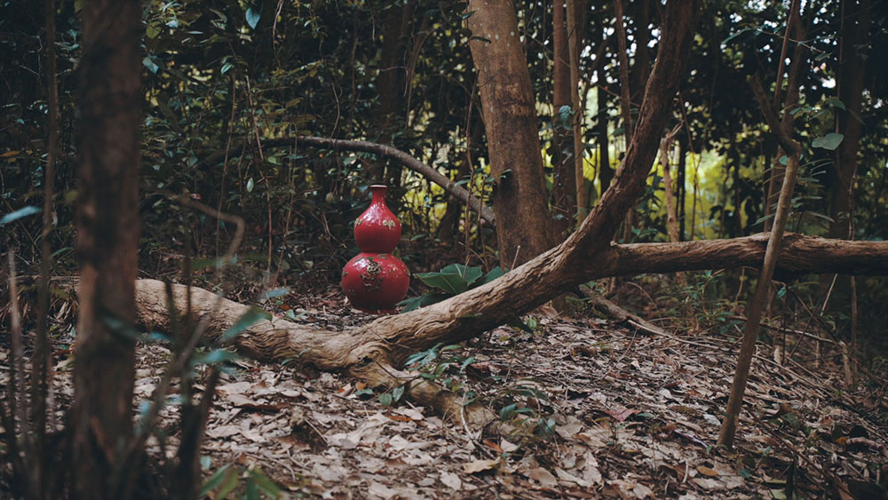 A bright red vase in the middle of the forest.