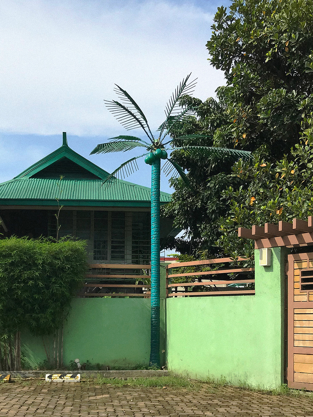 [Color-cooling] A fake coconut tree in one shade of green stands in front of a green building in Quezon City, housing the office of a coconute juice manufacturer.