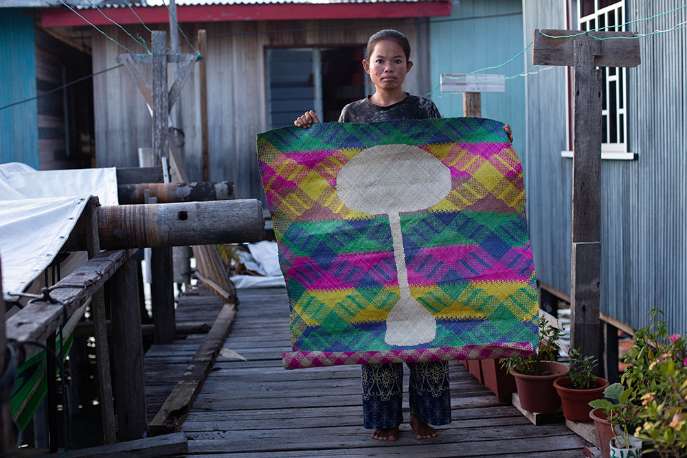 A weaver holding up a pandanus woven mat.